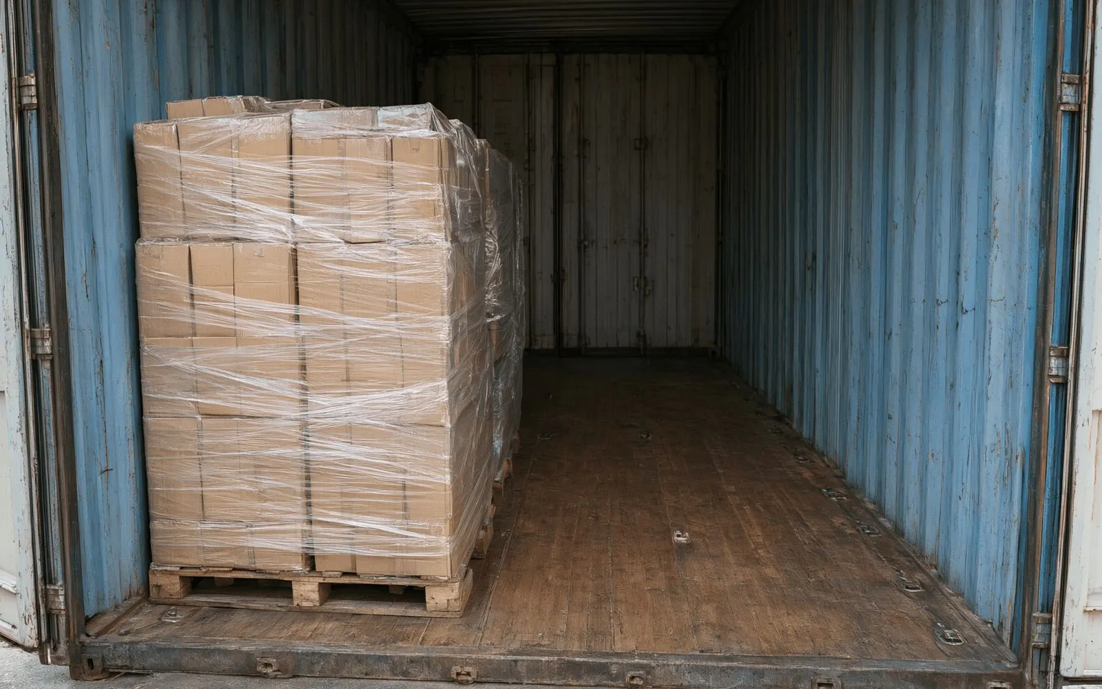 The interior of a shipping container loaded with wrapped cartons on pallets on one side, with empty floor on the other.